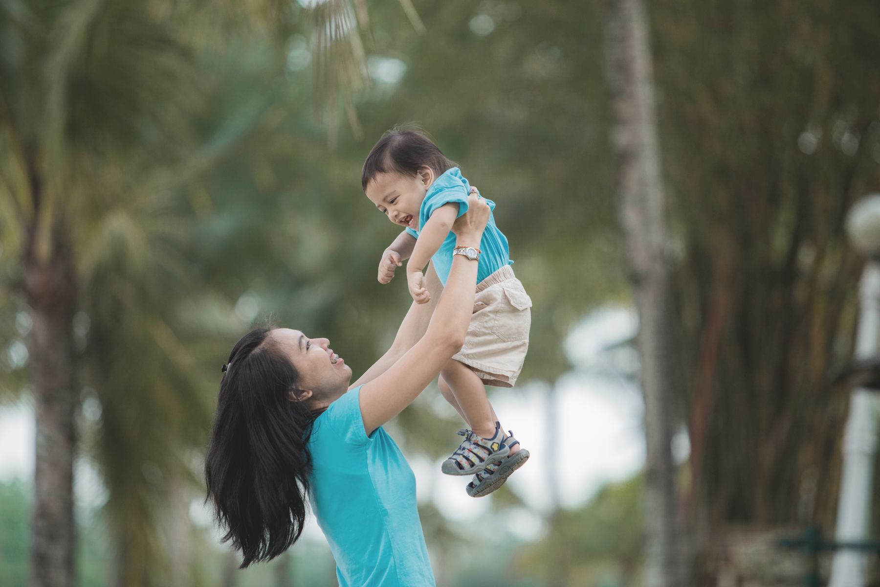 Seorang ibu mengangkat anaknya sambil tertawa di taman